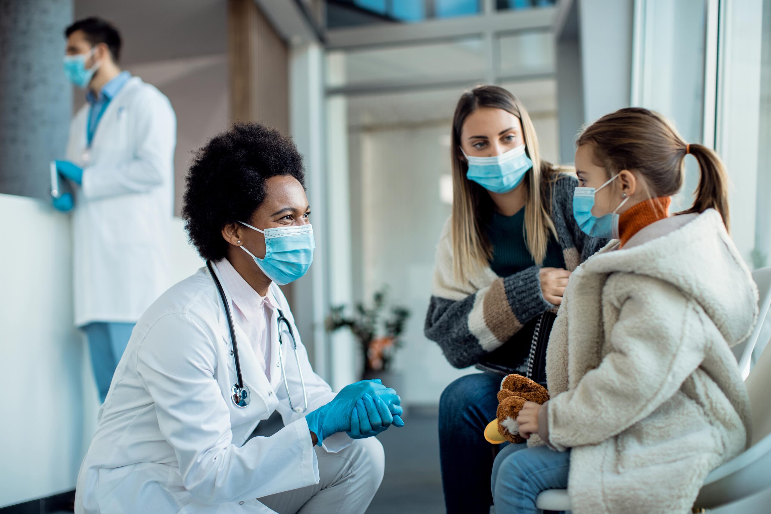 happy-african-american-female-doctor-talking-mother-daughter-waiting-room-medical-clinic-min